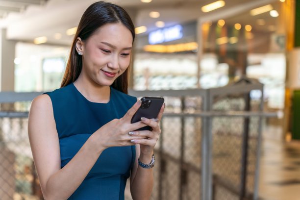 年轻的亚洲女商人女士与蓝色连衣裙使用她的手机室内购物中心自信图片下载