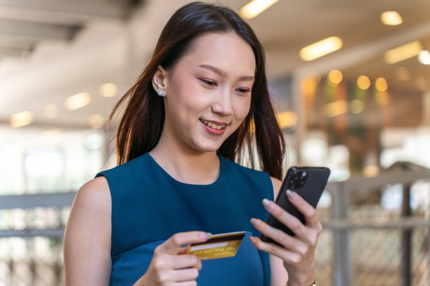 年轻的亚洲女商人女士，穿着蓝色衣服，用她的手机和信用卡在商场里自信地在线支付图片下载