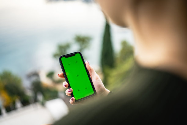 年轻的女孩使用手机与绿色屏幕在海边的阳台上的股票照片图片下载