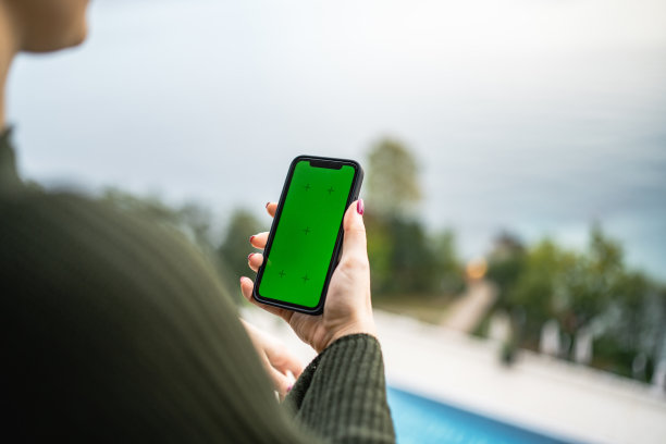 年轻的女孩使用手机与绿色屏幕在海边的阳台上的股票照片图片下载