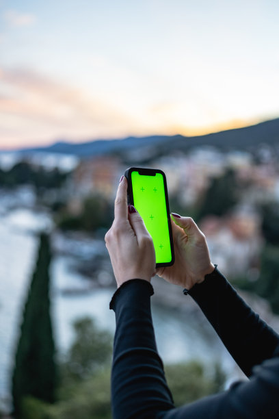 年轻的女孩使用手机与绿色屏幕在海边的阳台上的股票照片图片下载