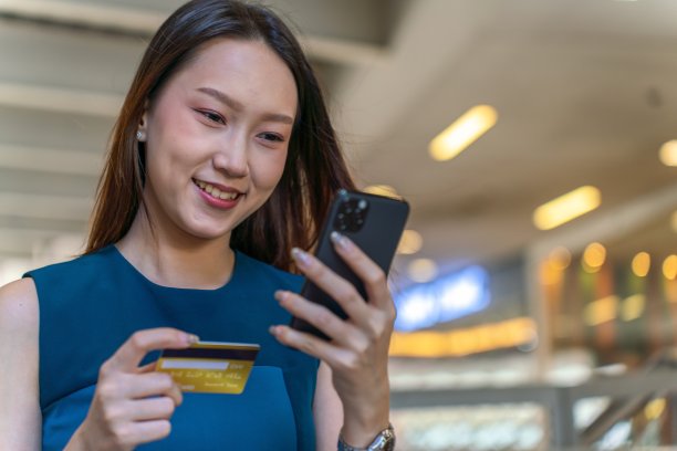 年轻的亚洲女商人女士，穿着蓝色衣服，用她的手机和信用卡在商场里自信地在线支付图片下载