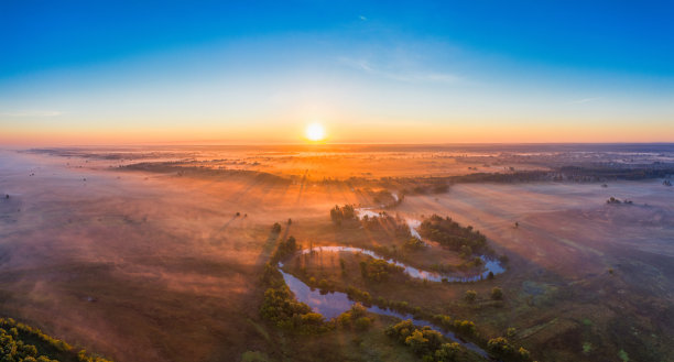 河的河道和弯道，在一片沼泽草地上。橙色的干草，被夏日的高温和晨雾烧焦。黎明时分的美景。无人机的观点。图片下载
