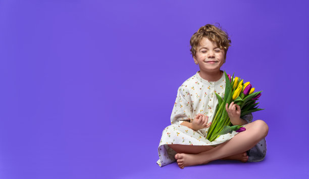 可爱的白人学前班女孩坐在紫色的背景冥想，手持一束黄色的郁金香。广告复制空间。春天清新积极的购物教育理念图片下载