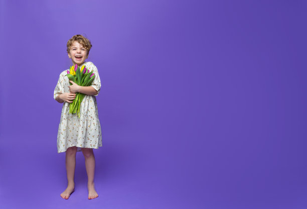 可爱的白人笑学前班女孩站在紫色的背景，手持一束黄色的郁金香。广告复制空间。春天清新积极的购物教育理念图片下载