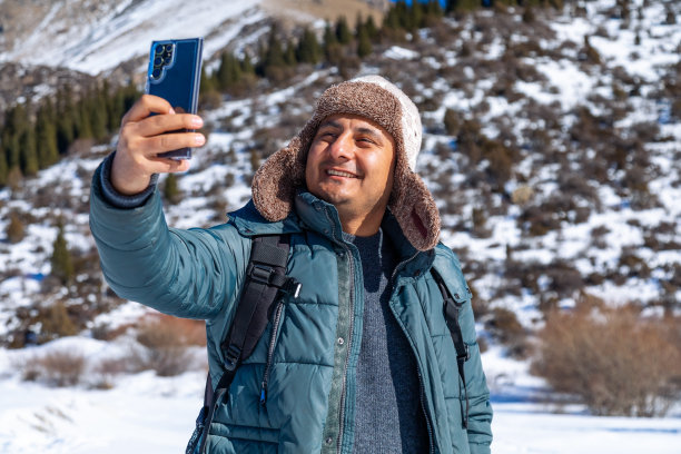 戴着冬季帽子的微笑男子在公园里用手机自拍的特写图片下载