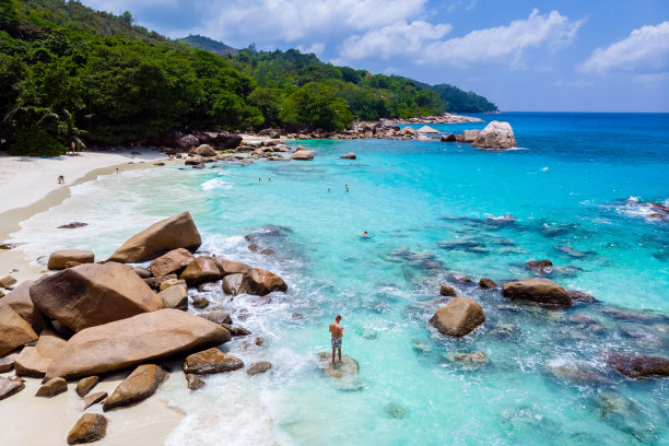 在塞舌尔普拉林岛的Anse Lazio海滩上，年轻男子站在白色的沙滩上，海水呈蓝绿色图片下载