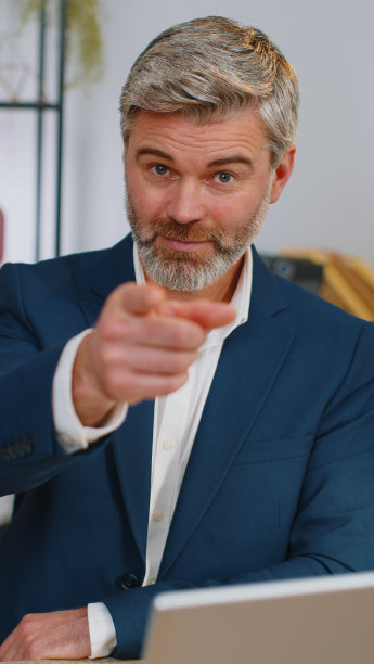 在办公室笔记本电脑上工作的商人指着相机，带着快乐的表情做出选择图片下载