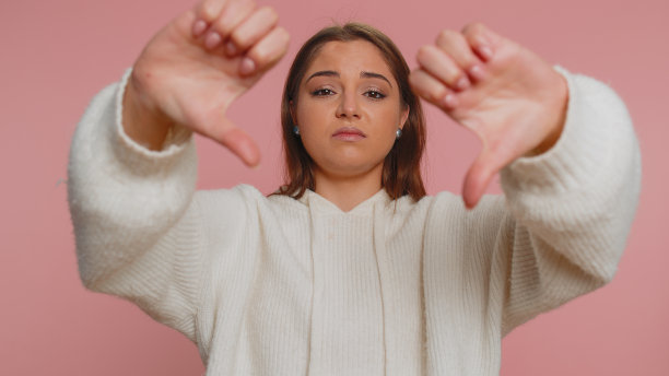 心烦的女人在白色毛衣显示拇指向下的手势，不赞成，不满的厌恶图片下载