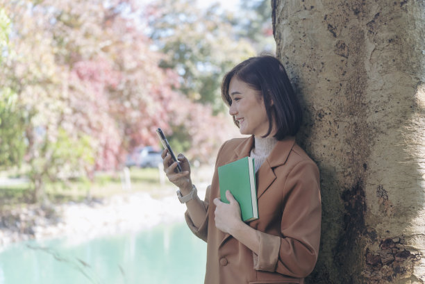 快乐的亚洲女人在绿色公园大自然的户外看书。读书杂志放松女人。休闲肖像女子微笑坐在绿色公园阅读电子书日记计划与快乐的脸图片下载