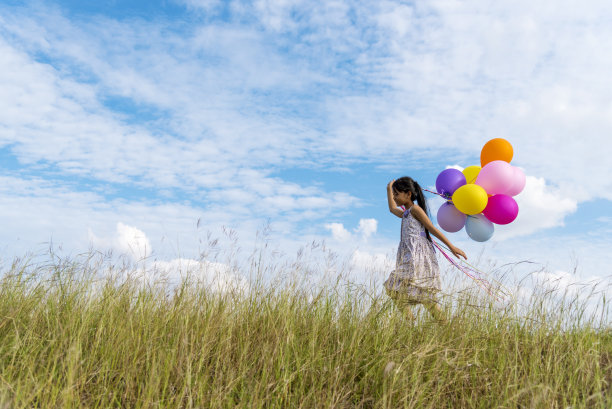 快乐可爱的女孩拿着气球在绿色的草地上奔跑，白云和蓝天与幸福。手握生机勃勃的气球玩生日派对快乐时光夏日阳光户外图片下载