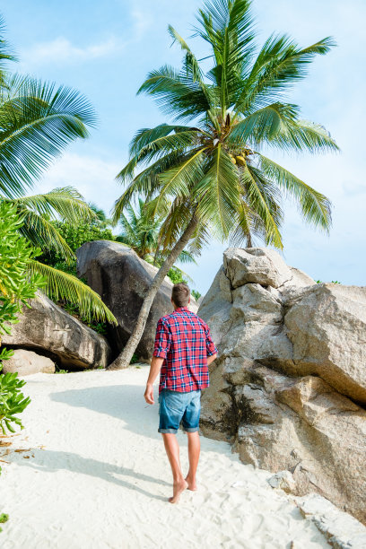 年轻男子走在塞舌尔群岛拉迪格阿金特海滩的白色热带海滩图片下载