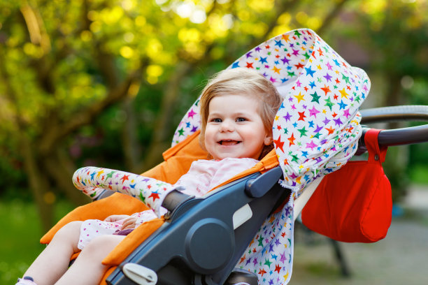 小可爱的微笑蹒跚学步的女孩坐在婴儿车或婴儿车的肖像，去散步。快乐可爱的宝宝在户外玩得很开心。健康的女儿。图片下载