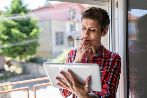 一个女人，成熟或高级女性，在明亮的日子里，在家靠窗吸烟，真实的人，复制空间，日常生活，不健康的习惯，尼古丁成瘾，严重周到地使用平板电脑图片下载