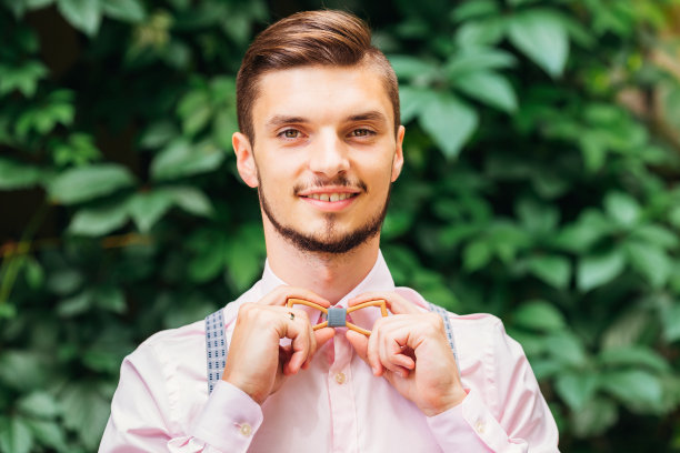 一个人在一个时尚的粉红色衬衫固定一个绿色树叶的背景木领结图片下载