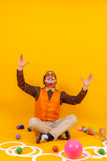 杂耍者穿着背心，用他的脸画着杂耍的物体坐在黄色的背景上，复制空间图片下载