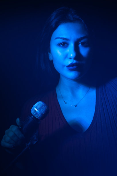 美丽的女人麦克风在蓝光背景。图片下载