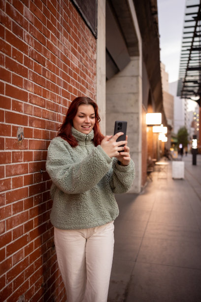 年轻女游客倚在红砖墙上自拍图片下载