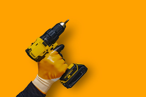 一名戴着手套的男子拿着一个电动螺丝刀，上面有一个橙色背景的电池。图片下载