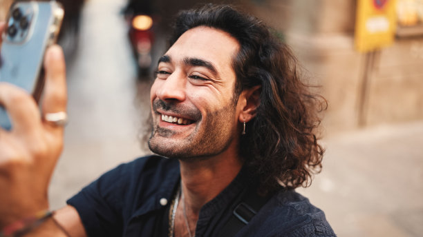 年轻有吸引力的意大利人长卷发和胡茬拍摄照片的老建筑。时髦的男人，耳朵上戴着耳环，拍着很多景点的链子。图片下载