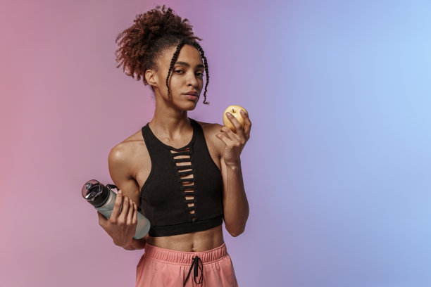 年轻女子在运动服拿着一瓶水和一个苹果在工作室背景锻炼后图片下载