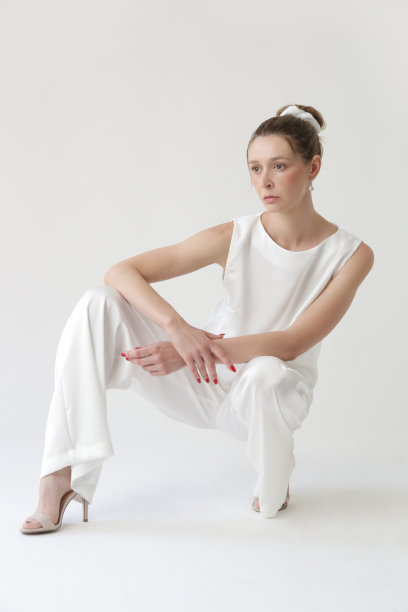 一系列的工作室照片，年轻的女模特在所有的白色丝绸装备，无袖上衣和宽腿裤图片下载