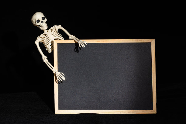 有趣的人类骨架在黑色背景上拿着一个空白的黑色空白。万圣节贺卡图片下载
