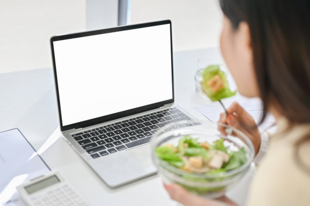 一个忙碌的亚洲女商人吃着健康的沙拉碗，在她的办公桌上吃午餐的特写图像图片下载