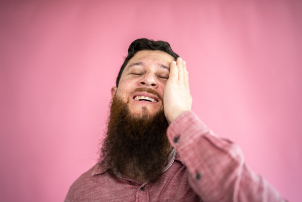 中年成年男子，双手放在脸上，在粉红色的背景上享受自己图片下载