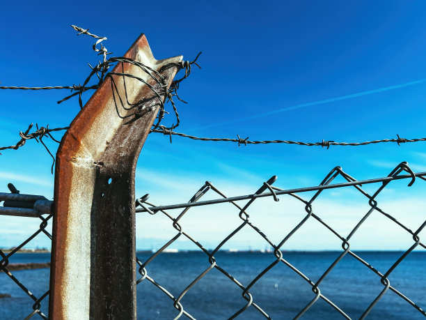 有刺的铁丝网包围着封闭的区域，湛蓝的大海和地平线上的天空是自由的象征图片下载