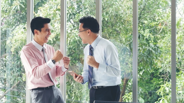 成功的商人得到了好消息手机智能手机。亚洲年轻商人举起手高兴地，微笑着，兴奋地从电话幸运地得到好消息。激动的两位商人ceo公司的成就图片下载