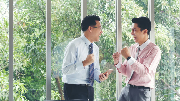 激动的两位商人ceo公司的成就。成功的商人得到了好消息手机智能手机。亚洲年轻商人举起手高兴地，微笑着，兴奋地从电话幸运地得到好消息图片下载