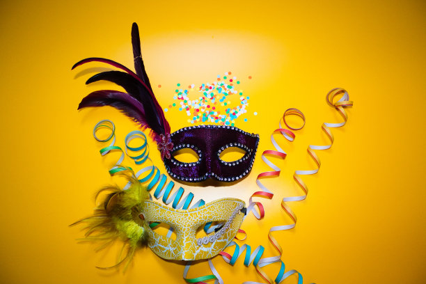 两个狂欢节面具，黄色背景上有五彩纸屑和卷纸图片下载