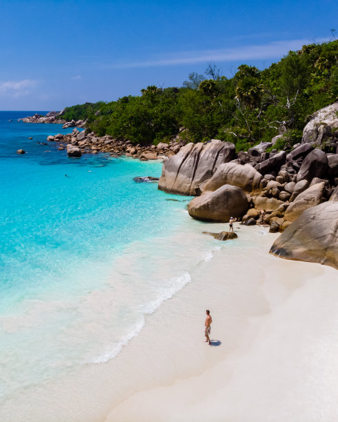 塞舌尔普拉林岛的安斯拉齐奥海滩上，一个年轻人在白色的海滩上，大海是蓝绿色的图片下载