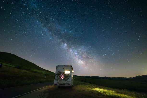 在星光下的美丽夜景中，一辆露营车在路上行驶图片下载