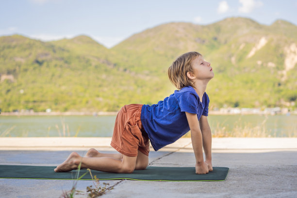 一个男孩在瑜伽垫上做瑜伽，背景是群山图片下载