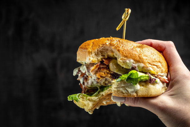 女性手拿着一个大的开胃咬汉堡在黑暗的混凝土背景，快餐和垃圾食品的概念，文字的地方图片下载