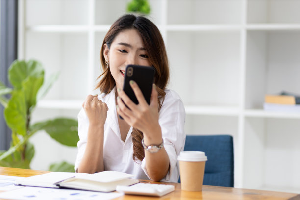 迷人的亚洲女性在办公室使用手机短信和智能手机通话。图片下载