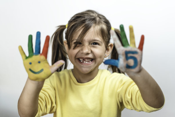 快乐的没有牙齿的小女孩与五个数字画在手上笑着玩-小女孩画她的手与笑脸和数字-数字五和童年的概念图片下载
