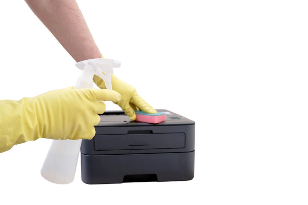 一名戴着黄色手套的清洁工正在打扫办公室，用一块海绵擦拭打印机和设备，它们被隔离在白色背景上图片下载