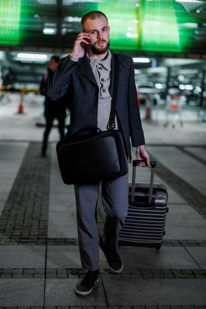 一个年轻的商人提着箱子离开机场，正在打电话。图片下载