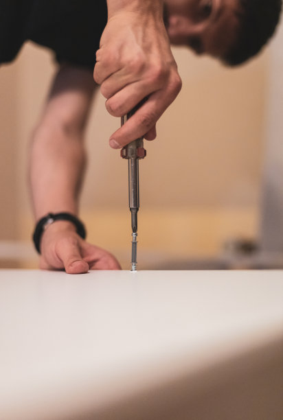 一个年轻人正在用螺丝刀把螺丝拧到一块木板上。图片下载