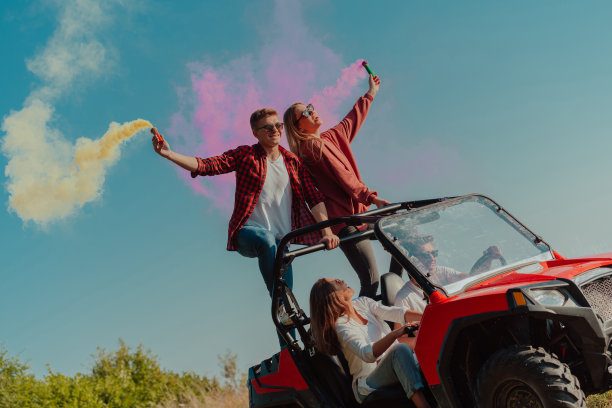 一群年轻的快乐兴奋的人享受着美丽的阳光，拿着五颜六色的火炬，开着越野车在山地自然。图片下载