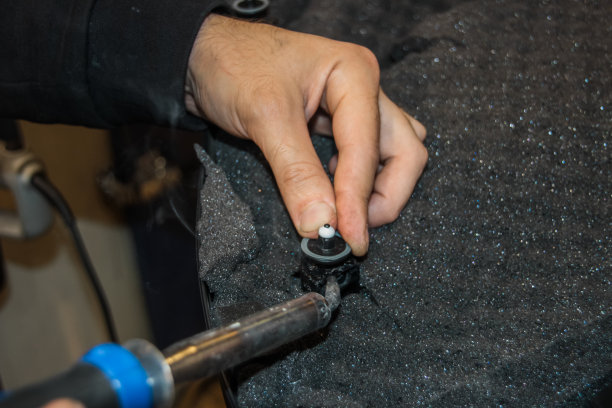 一个人在修理汽车内饰。这个人手里拿着一个烙铁，用它焊接零件。一个机械师用烙铁修理汽车。一名男子正在焊接门饰件的塑料夹子。图片下载