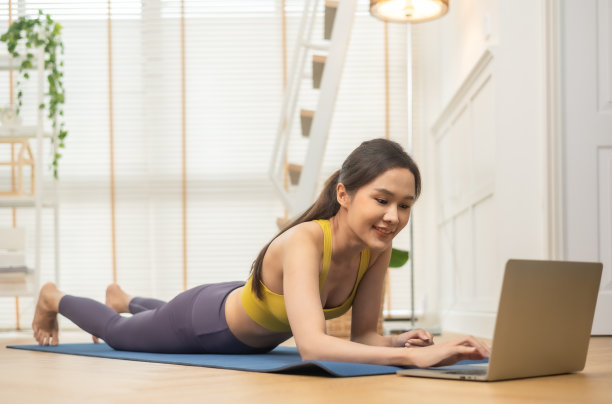 年轻的亚洲妇女在家里做瑜伽拉伸瑜伽。快乐的人呆在家里，在客厅做有氧运动，女孩做封锁活动，在家里和教练一起锻炼健康。图片下载
