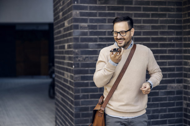 一个忙着微笑的聪明随意的商人走在街上留下语音信息。图片下载