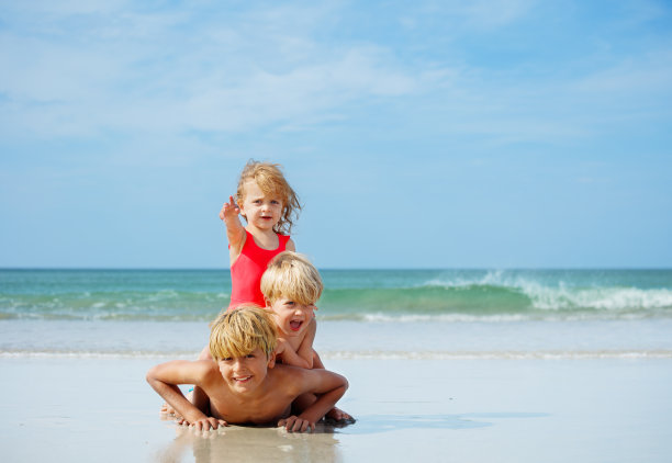 在沙滩上，三个孩子躺在另一个孩子上面图片下载