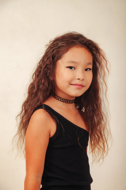 肖像亚洲小女孩长卷发摆姿势在白色背景，看着相机。工作室拍摄的时尚型相当小的时尚型模型。时尚教育理念。广告复制空间图片下载