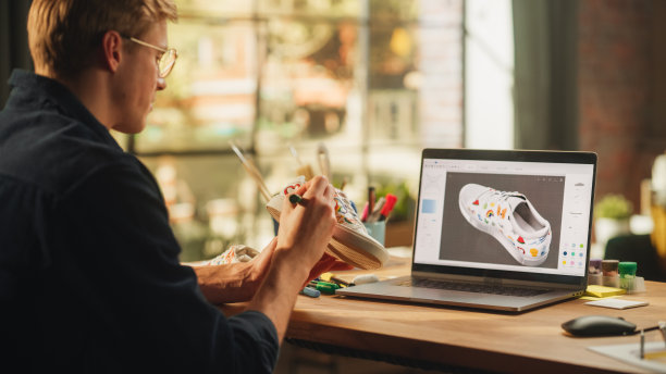 受启发的金发男子创建定制的鞋子模型，并在他的笔记本电脑上的编辑软件中查看3D原型。艺术和独特的DIY对象为个人风格的概念。图片下载