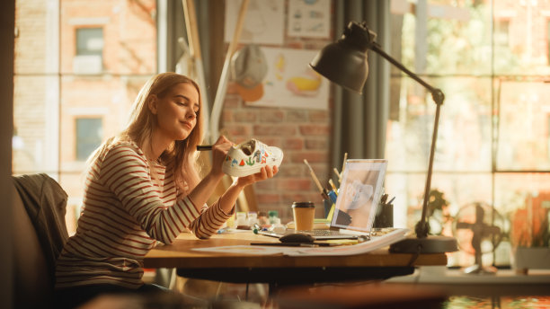 女创意设计师工作在鞋子和使用笔记本电脑在Loft办公室工作室。时尚艺术家定制一双运动鞋与鞋类艺术。新一代创意概念。图片下载